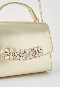 Gold metallic handbag with a smooth leather texture, featuring a jeweled floral accent comprising multiple clear gems on the front.
