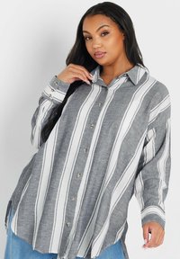 Camisa de botones a rayas gris y blanca hecha de tela ligera; cuenta con un cuello, tapeta de medio botón y mangas largas con puños.