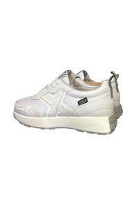 Sneakers bianchi realizzati in materiale strutturato, con colletto imbottito, lacci e una suola spessa con etichetta del logo sul lato.