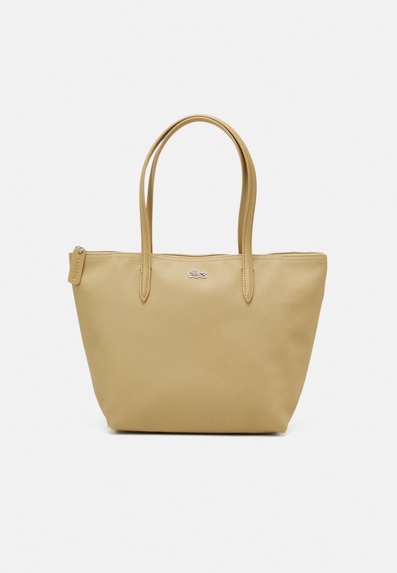 Gul totebag laget av teksturert syntetisk materiale, med to lange håndtak og glidelås-lukking. Emblemdetalj på forsiden.
