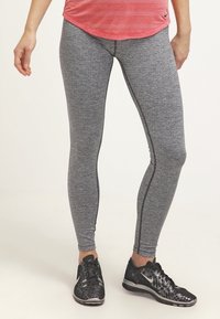 Szare legginsy sportowe o heatherowym wykończeniu, z dopasowanym krojem i kontrastowymi szwami po bokach. W połączeniu z czarnymi butami sportowymi.