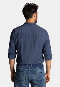 Navyblauwe overhemden met kraag van geweven stof, opgerolde mouwen en verticale naaddetails. Gecombineerd met vervaagde blauwe spijkerbroeken met dubbele achterzakken.