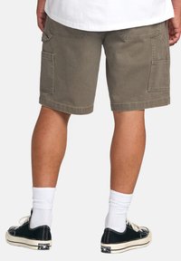 Shorts cargo verde măsliniu cu două buzunare laterale, o croială relaxată și un tiv care se termină la mijlocul coapsei, asortați cu adidași negri și șosete albe.