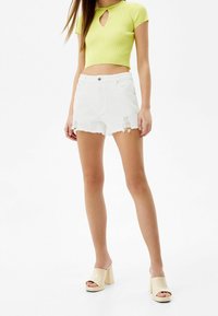 Limevihreä ribbed crop-top avocleikkaustyylillä, yhdistettynä valkoisiin kuluneisiin denim-shortseihin ja beigeihin avonaisiin korkokenkiin.