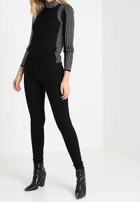 Musta pitkähihaisena paita, jossa on teksturoitu kuvio hihoissa, yhdistetty mustiin slim fit -housuihin ja kiiltäviin nilkkabootseihin. Sujuva kangas ja istuva muotoilu.