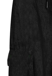 Zwart denim stof met zichtbare stiksels, met een rechthoekige klepzak en een deel van een zilveren rits aan de rechterkant.