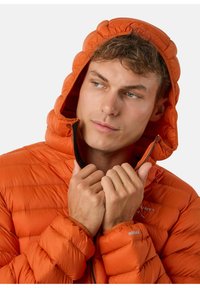 Helderoranje geïsoleerde jas met een capuchon, voorzien van gestikte patronen en een rits aan de voorkant. Geaccentueerd met elastische manchetten en branding.