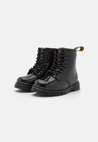 Stivali alla caviglia in pelle verniciata nera con punta rotonda, dotati di lacci frontali e di un pratico passante giallo. Sole in gomma texture con dettagli di cucitura.