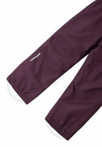 Pantalones impermeables color burdeos con puños elásticos, que presentan un acento reflectante en el muslo y un acabado suave y mate.
