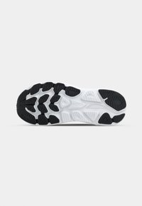 Semelle de chaussure de sport noire et blanche présentant un motif de grip en caoutchouc texturé, avec des éléments de bande de roulement proéminents pour l'adhérence et la durabilité.