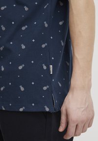 Tamnoplav T-shirt z malim vzorcem ananasa in diamanta, kratkimi rokavi, stranskimi razporki in tkano blagovno oznako na robu.
