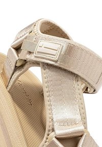 Sandalia beige con correas texturizadas, plantilla acolchada y una pequeña hebilla ajustable. El material parece ligero y duradero.