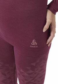 Maroon athletic top and leggings made from smooth fabric, featuring a geometric pattern on the lower leg and a logo on the side.