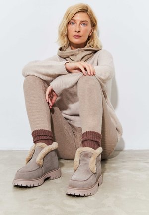 Gray suede ankle boots with faux fur trim, rubber soles, and zigzag pattern. Styled with beige ribbed sweater and pants.