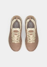 Lystebrune sportssko med cremefarvede detaljer, mesh-overdel, perforeret design og neutrale snørebånd; med rund tå og polstret sål.