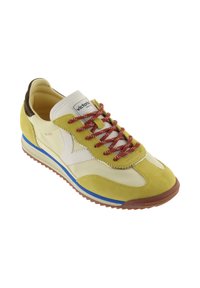 Sneaker giallo e beige con accenti marroni e bianchi, lacci rossi con puntini bianchi, striscia blu sulla suola e etichetta con logo sulla linguetta.