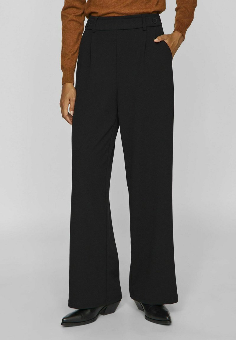 Pantalons larges noirs avec un devant plat, deux boutons et des poches latérales. Fabriqués à partir d'un tissu lisse et texturé.