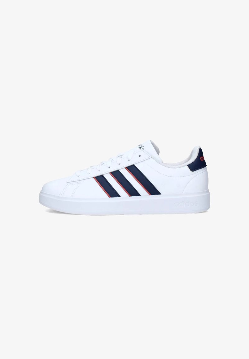 Zapatilla deportiva blanca con tres rayas marinas y acentos rojos; parte superior de cuero suave, suela plana, punta redonda y diseño con cordones.