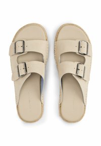 Sandali beige con due ampie cinghie in suede e fibbie argentate. Presentano una suola piatta con un bordo intrecciato simile al juta e una soletta liscia.