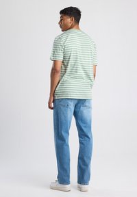 Maglietta a righe verde e bianca con un taglio rilassato, abbinata a jeans in denim blu chiaro e sneakers bianche, vista da dietro.