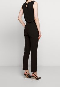 Černý bezrukávový top s detaily ve tvaru klíčové dírky, kombinovaný s upnutými černými kalhotami a otevřenými černými podpatky. Hladká látka a štíhlý silueta.