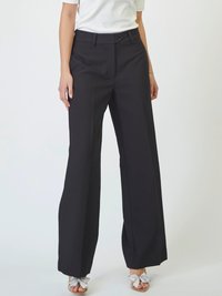 Pantaloni neri a gamba larga con davanti piatto e chiusura a bottoni. Realizzati in un tessuto liscio e strutturato. Indossati con una maglietta bianca e scarpe con dettagli argentati.