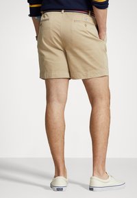 Shorts caqui con un diseño ajustado, hechos de algodón, que cuentan con dos bolsillos traseros y una textura suave, combinados con zapatillas de color claro.