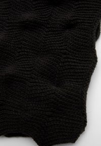 Tessuto nero lavorato a maglia con un motivo a zigzag testurizzato, mostrato in primo piano su uno sfondo bianco.