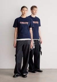 Camisetas de algodón azul marino con el logo "Tommy Jeans", combinadas con pantalones anchos de mezclilla oscura y zapatos negros; modelo con una camisa de cuadros atada a la cintura.