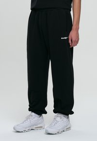 Svarta sweatpants med elastisk midja och sidofickor, med en vit logodetalj. Matchas med vita sportiga sneakers med synlig luftdämpning.