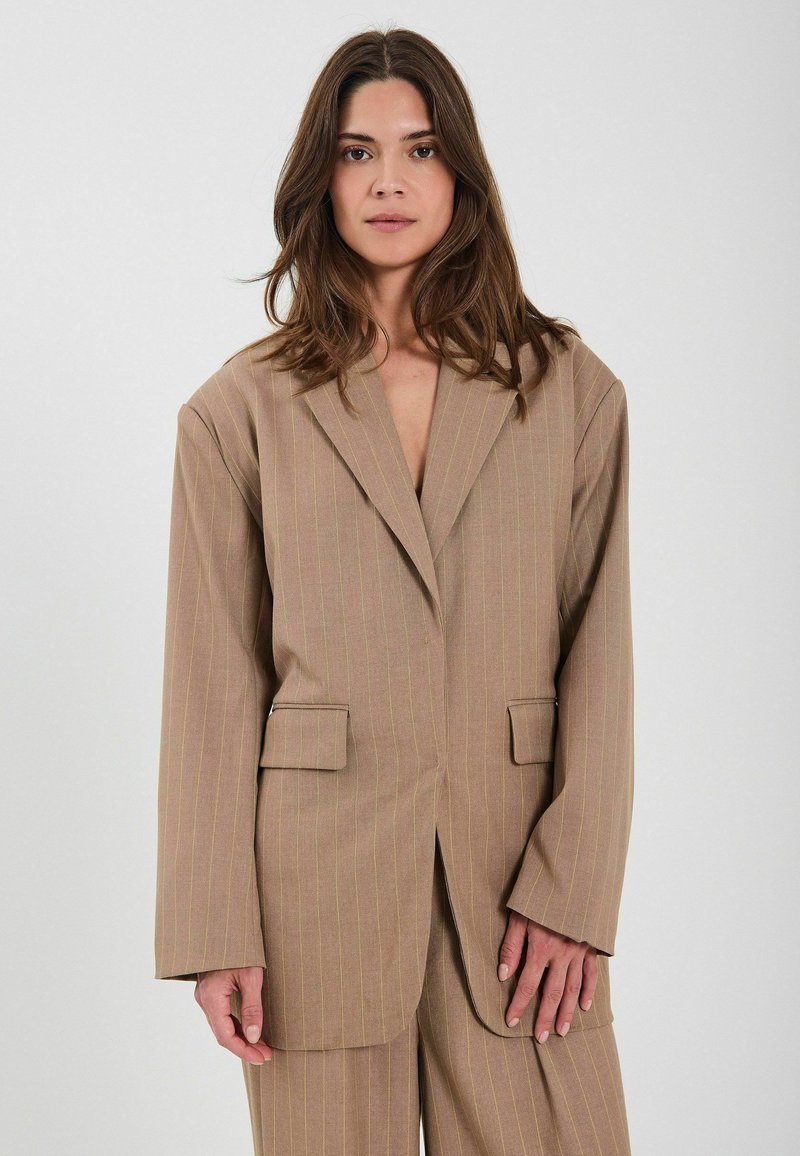 Beige blazer med pinstriber og slåede lommer, to frontlommer og brede ærmer, der pryder subtile lodrette linjer i en lidt lysere nuance.