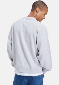 Grå hettegenser med rund hals og ribbestrikkede ermer, med en avslappet passform og myk tekstur, båret over en hvit t-skjorte og blå jeans.