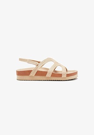 Sandalias de tiras trenzadas en color beige con una suela gruesa en tono marrón. Presentan una suela plana y un diseño entrelazado para un ajuste seguro.