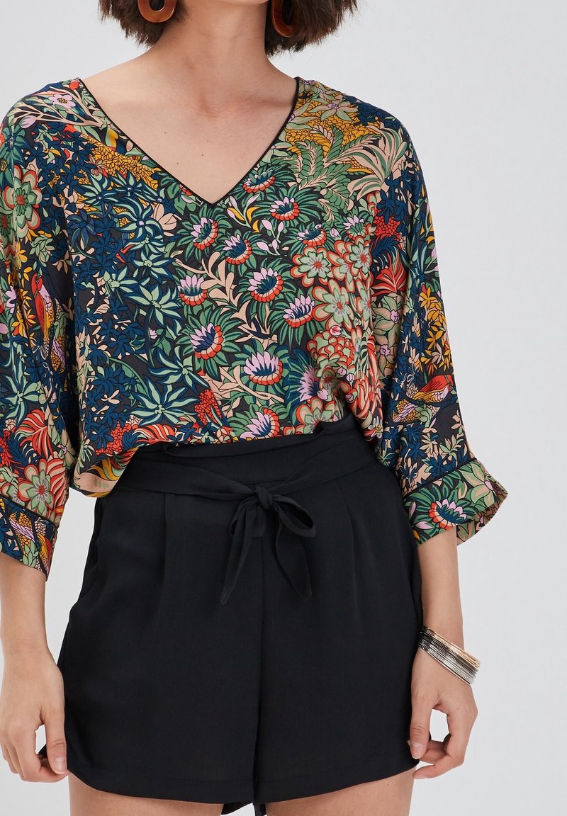 Top w kwiatowy wzór z dekoltem w serek, czarne szorty z wiązanym pasem. Top ma żywe kolory na ciemnym tle.
