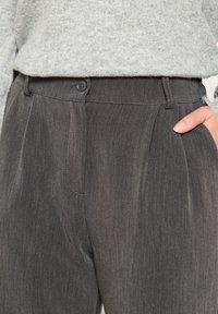 Gray tailored trousers with a subtle pinstripe pattern, featuring a button closure, pleated front, and side pockets. Textured fabric.