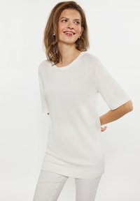 Hvid kortærmet sweater med rund halsudskæring, lavet af et struktureret strikstof, som har en løs pasform og sideslidser i kanten.