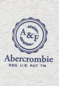 Tessuto grigio con un logo circolare blu navy. Presenta le lettere "A & F" e la parola "Abercrombie" in un carattere audace in stile vintage.