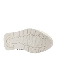 Semelle en caoutchouc blanche de sneaker avec un motif de semelle texturé, présentant des éléments de traction circulaires et un logo de marque. Bords lisses et arrondis.