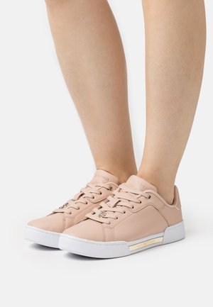 Jasnoróżowe syntetyczne skórzane sneakersy z białymi gumowymi podeszwami. Mają sznurówki, markowy język oraz złoty akcent z boku.