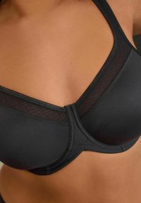 Soutien-gorge noir en tissu doux, avec un design en V, des panneaux en maille près des bretelles et un armature structurée pour le soutien.