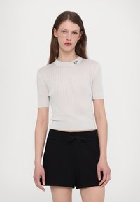 Kortärmad vit ribbad topp med en åtsittande design, med rund halsringning och liten "A|X"-logotyp på kragen, matchad med svarta shorts.