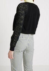 Svart kortärmad tröja med spetsmönstrade ärmar, bärs över rutiga byxor. Har en enhetlig baksida och ribbad halsringning.