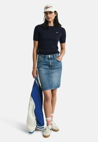 Marineblauwe kabelgebreide top met korte mouwen, lichte denim kokerrok, witte pet, crèmekleurige sneakers, gestreepte rood-witte sokken, blauw-witte jas.