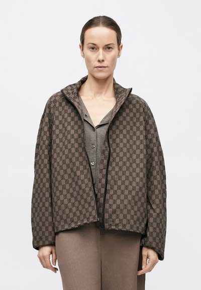 Jachetă maro cu model, cu guler înalt, închidere cu fermoar și siluetă lejeră, prezentată peste un top gri și pantaloni asortați.