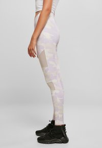 Leggings à motif camouflage dans des teintes pastel avec une coupe ajustée. Détails en mesh sur les côtés, associés à des chaussures de sport noires.