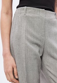 Hallid kohandatud püksid tekstuurse kangaga, mis on varustatud lameda eesosaga, küljetaskutega ja sirge säärekujundusega. Nähtav õmbluste detail.