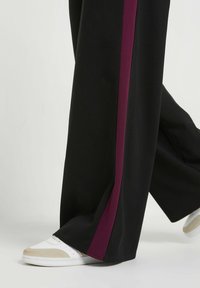 Pantaloni neri a gamba larga con una striscia laterale bordeaux, realizzati in tessuto morbido, abbinati a sneakers bianche e beige. Design semplice e moderno.