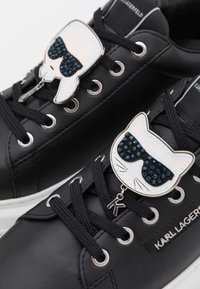 Le sneakers in pelle nera presentano un distintivo a forma di gatto con occhiali da sole, decorato con strass blu. Include lacci neri e dettagli in metallo argentato.