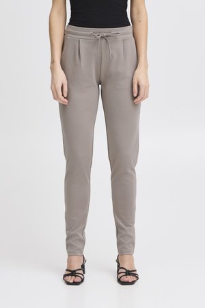 Pantaloni jogger color talpa a taglio aderente con vita con coulisse, indossati con sandali neri con tacco e cinturini e un top nero senza maniche.