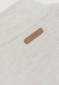 Tejido beige con una textura sutil y una etiqueta rectangular de cuero marrón cosida, embellecida con la palabra "REISS".